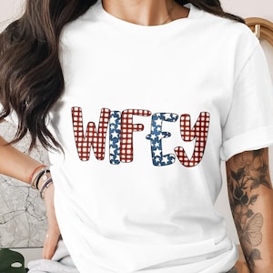 May include: White t-shirt with the word "WIFEY" in a playful font. The letters are decorated with red and white gingham and blue stars, creating a patriotic design. A casual and comfortable top.