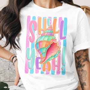 Puede incluir: Camiseta blanca con un diseño de concha marina colorida y las palabras "SHELL YEAH!" en colores pastel. El diseño incluye tonos rosa, azul, naranja y verde, perfecto para un tema de playa o verano.