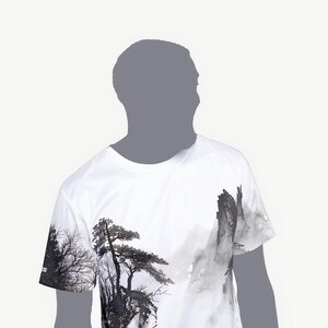 May include: A white short-sleeve t-shirt featuring a black and gray ink wash style graphic print. The design depicts a detailed landscape with tall pine trees and jagged mountain peaks, extending across the front and onto the right sleeve.