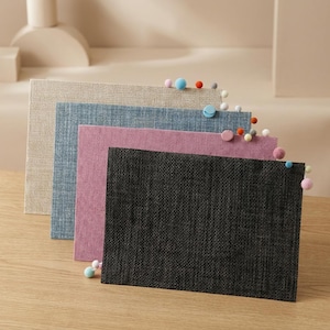 Puede incluir: Un conjunto de cuatro tableros de visualización rectangulares en beige, azul, rosa y gris oscuro, cada uno con una superficie de tela texturizada. Pequeños alfileres de pompones de fieltro de colores están sujetos a los bordes superiores y laterales.
