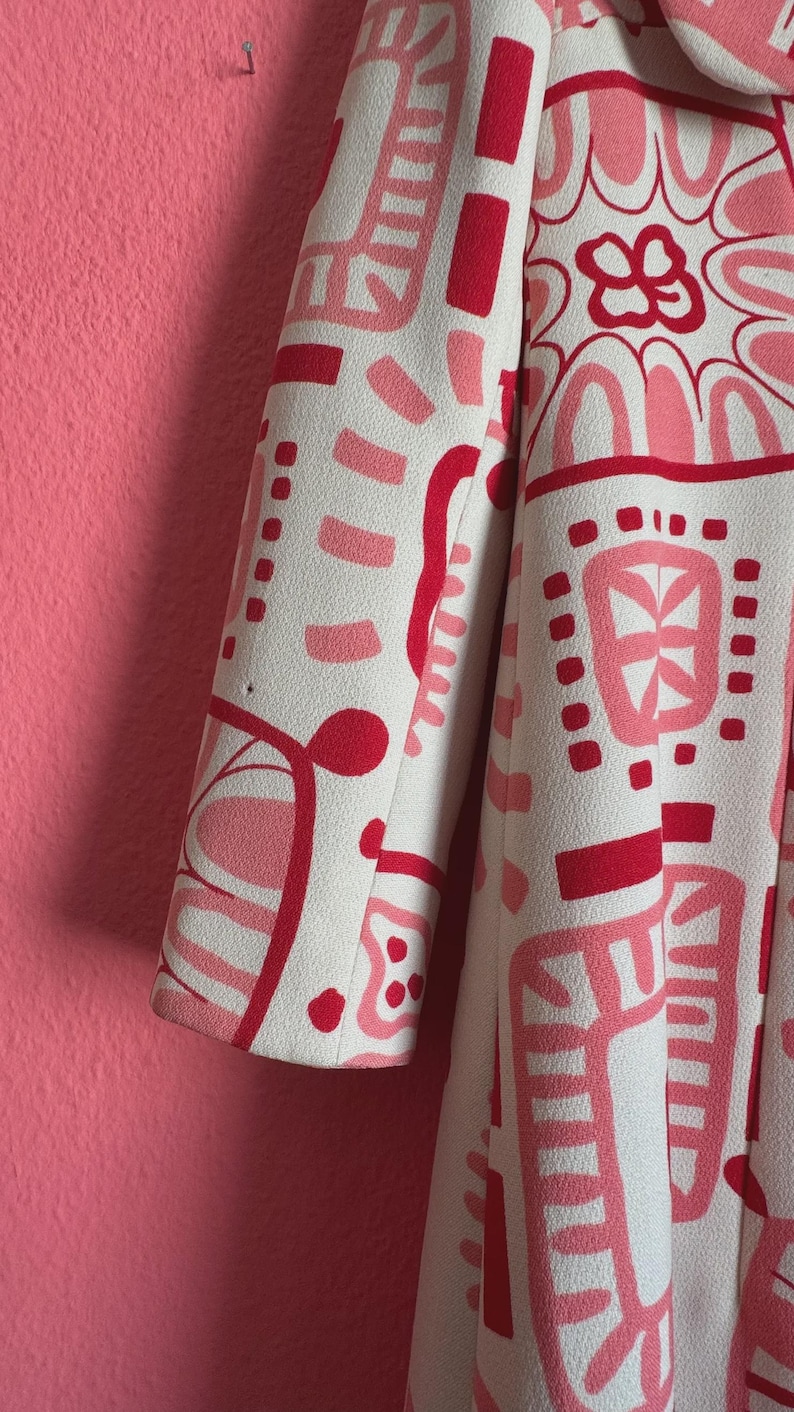 May include: A long-sleeved coat featuring an off-white base color with a bold, abstract graphic pattern in shades of bright red and soft pink. The design consists of various geometric shapes, curved lines, and floral-inspired motifs.