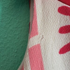 May include: A sleeveless garment featuring a textured off-white fabric with a bold red and pink geometric pattern. The design includes a solid red section at the top and a light pink lining visible along the armhole seam, showcasing a woven textile.