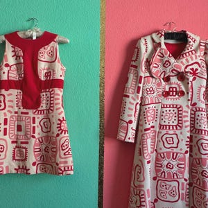 May include: A sleeveless dress and a long-sleeved coat, both featuring a cream base with a repeating red and pink geometric pattern. The dress has a solid red panel on the chest, while the coat includes a wide collar and red button closures.