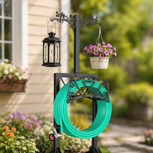 May include: A black metal garden hose holder with a decorative scroll design, holding a coiled green hose. A black lantern hangs from a decorative arm, and a white hanging basket with pink flowers is also attached.