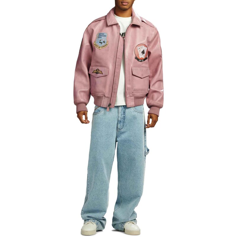 May include: A dusty rose bomber jacket with patches and a zipper closure. The jacket is paired with light blue, baggy jeans. The model is wearing a white t-shirt and white sneakers.