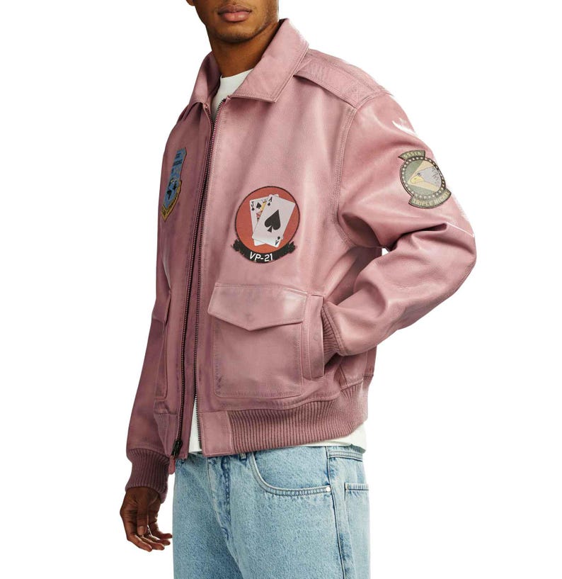 May include: A dusty rose leather jacket with a zip-up front, two front pockets, and a ribbed hem. The jacket features embroidered patches, including playing cards and a military emblem. The text "VP-21" is visible on one patch.