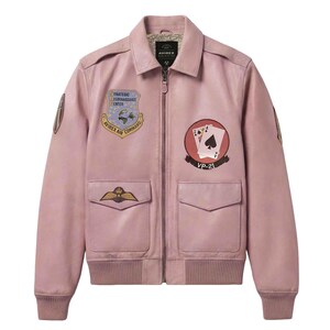 May include: A pink leather bomber jacket with multiple patches. The jacket features a collared neckline, a zipper closure, and two front pockets. Patches include the text "Strategic Reconnaissance Center" and "Avirex Air Command".