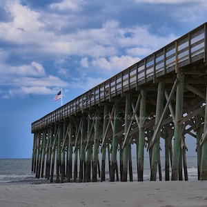 Amerikaanse vlag wappert over pier | Patriottische strandkunst aan de muur | Dramatische kustfotografie met een laag camerastandpunt