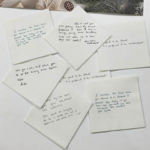 May include: A collection of white square paper napkins featuring handwritten black ink messages. The notes include personal sentiments such as I remember the first time you showed up in Montauk, Can't wait for our future, and It's good to be loved.
