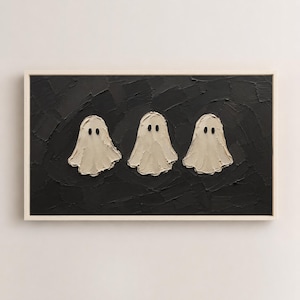 May include: A rectangular wall art piece featuring three off-white, textured ghost figures with black oval eyes centered against a thick, impasto-style black background. The artwork is enclosed in a simple, light-colored wooden frame.