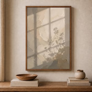 May include: A rectangular wall art piece in a dark wood frame featuring a textured, beige and cream impasto surface. The artwork displays a soft, dark shadow of a plant and window pane cast across the layered, uneven paint strokes.