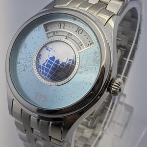 May include: A silver wristwatch with a light blue face featuring a globe design. The watch has a silver band and a unique dial with numbers and a small globe graphic. The text "U2" is visible on the watch face.