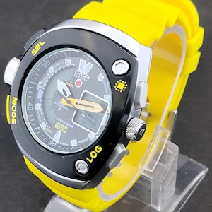 May include: A Citizen Eco-Drive dive watch with a black face, yellow accents, and a yellow rubber strap. The watch features a digital display and multiple buttons. The watch is displayed on a clear plastic stand.