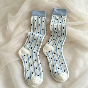 May include: A pair of white socks with a light blue cuff and vertical stripes. The socks have black polka dots and light blue stripes running down the length of the sock.