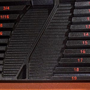 May include: A black stepped gauge tool with red markings. The tool has fractional inch measurements from 1/8 to 3/4 on one side and numbered measurements from 10 to 19 on the other. The tool is designed to measure the size of objects.