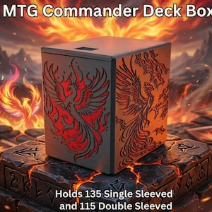 Puede incluir: Caja de mazo MTG Commander con diseño de fénix. La caja es gris oscuro con ilustraciones de fénix rojas en los lados. Contiene 135 cartas con una funda o 115 con doble funda. El fondo presenta llamas y una superficie rocosa.