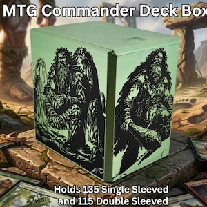 Op de afbeelding: Een lichtgroene MTG Commander Deck Box met zwarte illustraties van een bebaarde figuur. De doos biedt ruimte aan 135 kaarten met enkele sleeves of 115 met dubbele sleeves. De tekst "MTG Commander Deck Box" staat bovenaan.