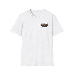 Op de afbeelding: Wit T-shirt met een ronde hals en korte mouwen. Een kleine afbeelding op de linkerbovenborst toont een groep figuren en de tekst "CRYPTED COFFEE CLUB" in een donkere kleur.