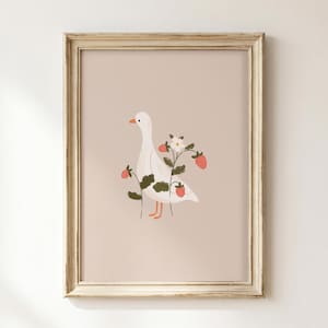 May include: A framed wall art print featuring a white goose standing among green strawberry plants with red berries and a single white flower. The illustration is set against a solid light beige background and enclosed in a light wood frame.