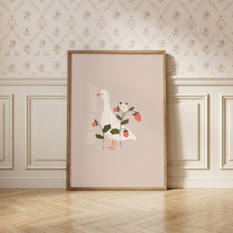 May include: A framed vertical wall art print featuring a white goose with an orange beak and feet, surrounded by green strawberry plant stems with red strawberries and a single white flower, set against a solid light beige background.
