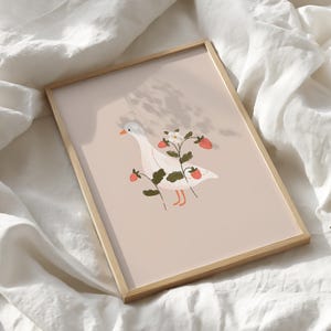 May include: A rectangular framed print featuring a white goose with an orange beak and feet, standing amidst green strawberry plants with red berries and a white flower, set against a solid light beige background within a light wood frame.