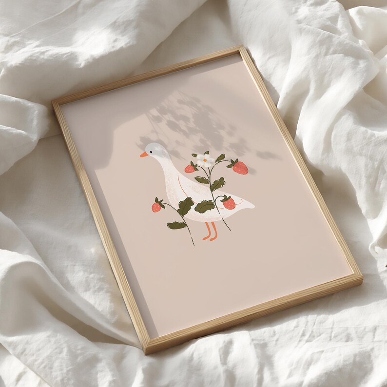 May include: A rectangular framed print featuring a white goose with an orange beak and feet, standing amidst green strawberry plants with red berries and a white flower, set against a solid light beige background within a light wood frame.