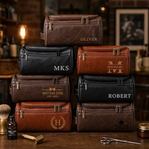 Puede incluir: Una pila de neceseres de cuero personalizados en tonos marrones y negros. Cada bolsa tiene cierre de cremallera y está grabada con nombres, iniciales o frases como "BEST DAD EVER" y "CLASS OF 2025".