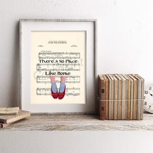 May include: Framed artwork featuring sheet music with the text "There's No Place Like Home" and illustrations of red shoes. The artwork is displayed on a wooden shelf with books and a clock.