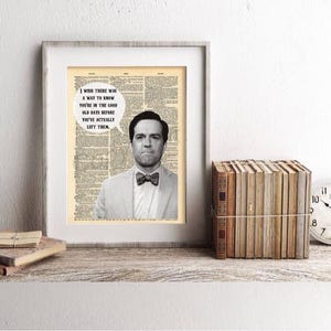 May include: Framed print featuring a man in a suit and bow tie, with a quote bubble. The background is a vintage newspaper print. A stack of books and a clock are on the shelf below.