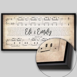 May include: Framed artwork featuring sheet music with lyrics and the names "Eli & Emily" and the date "10.17.21" in elegant script. The artwork has a vintage, aged paper appearance, and is encased in a black frame.