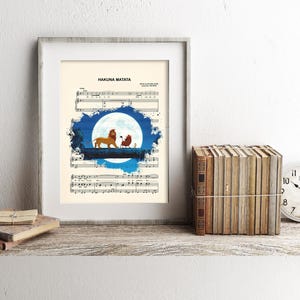 May include: Framed art print featuring sheet music with the words "Hakuna Matata." The artwork depicts a lion and a meerkat silhouette against a blue and white background, resembling a moon. A stack of books and a clock are on the shelf.
