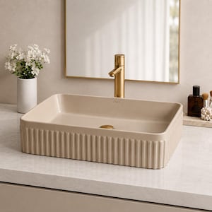 Puede incluir: Un lavabo rectangular beige con un exterior acanalado. Se instala un grifo y un desagüe dorados. El lavabo está sobre una encimera de color claro, con un espejo y accesorios en el fondo. El lavabo está etiquetado como "VIGO".