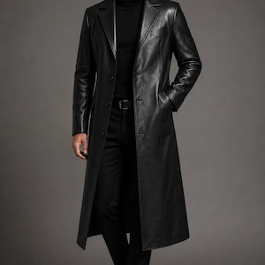 May include: A long black leather coat featuring a notched lapel, a button-front closure, and two side pockets. The coat is worn over a black turtleneck sweater, black trousers with a belt, and black leather boots, creating a monochromatic look.