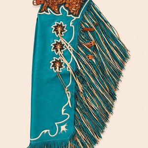 May include: A teal leather chap featuring a brown leather yoke with intricate floral tooling. The leg panel displays three star-shaped appliqués and long, layered fringe in both teal and cream colours. A brown leather belt with a metal buckle secures the top.