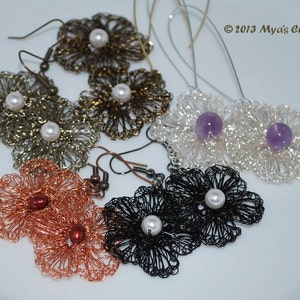 May include: Six pairs of earrings with flower-shaped wirework designs. Each pair features a different color and embellishment, including pearls, amethyst stones, and copper beads.