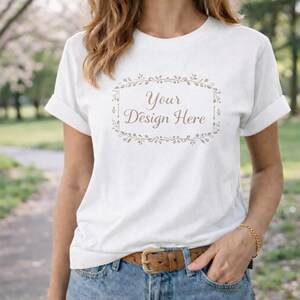 May include: A white t-shirt with rolled sleeves and the text "Your Design Here" within a decorative frame. The shirt is worn with blue jeans and a brown belt. A gold bracelet is visible on the wrist.