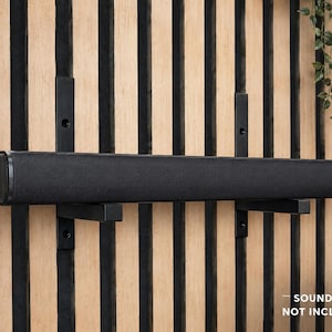 Peut inclure: Un support mural noir pour barre de son composé de deux supports métalliques verticaux avec des bras horizontaux. La quincaillerie noire mate est conçue pour maintenir un appareil audio rectangulaire. Le texte "SOUNDBAR NOT INCLUDED" est visible.
