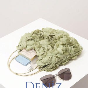 May include: A light green floral handbag with a gold handle, sunglasses, a blue phone, and a small cosmetic case. The bag is filled with items and sits on a white surface. The text "DENIZ BAG STYLE" is at the bottom.
