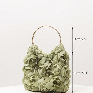 May include: A sage green handbag, 24cm wide, 18cm tall, and 1cm thick, is covered in fabric roses. It has a gold-coloured, circular handle and is 14cm tall. The bag is on a white surface.