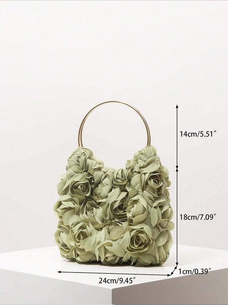 May include: A sage green handbag, 24cm wide, 18cm tall, and 1cm thick, is covered in fabric roses. It has a gold-coloured, circular handle and is 14cm tall. The bag is on a white surface.