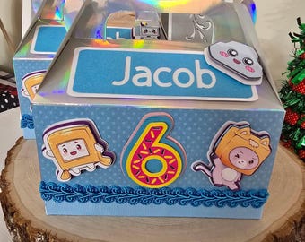 May include: A blue birthday gift box with the name "Jacob" on it, decorated with cartoon characters and the number "6". The box has a holographic handle and is sitting on a wooden surface.