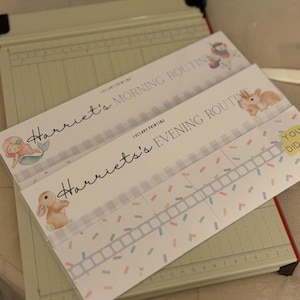 May include: Two rectangular paper charts titled Harriet's Morning Routine and Harriet's Evening Routine. The charts feature illustrations of a unicorn, a mermaid, and a rabbit, with a grid for tracking tasks and colorful confetti-like accents.
