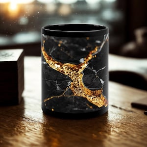 May include: Black coffee mug with a marble design featuring gold accents. The mug has a black rim and base, and the marble pattern is a mix of black and white with gold veining. The mug is cylindrical and sits on a wooden surface.