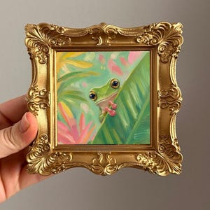 Tiny original oil painting of a sweet green frog peeking from behind a tropical leaf. This miniature 3x3 inch artwork is hand painted with visible oil texture, soft brushstrokes, and fresh pastel tropical colors.

A charming small artwork for frog lovers, whimsical home decor, dopamine decor, nursery shelves, gallery walls, desk styling, or a unique handmade gift.
