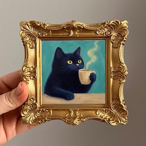 以下が含まれることがあります： コーヒーカップを持つ黒猫の絵画。猫は黄色い目をし、背景はターコイズブルー、金色のフレームは装飾的です。湯気が立ち上っています。