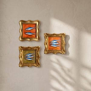 May include: Three framed fish paintings with ornate gold frames. Each painting features a different arrangement of blue and white fish against a colorful background. The frames are square with decorative edges, creating a classic aesthetic.