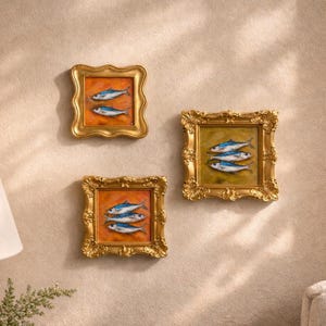 May include: Three framed fish paintings. Each painting features a different arrangement of blue and white fish against a warm orange or green background. The ornate gold frames add a touch of elegance to the artwork.