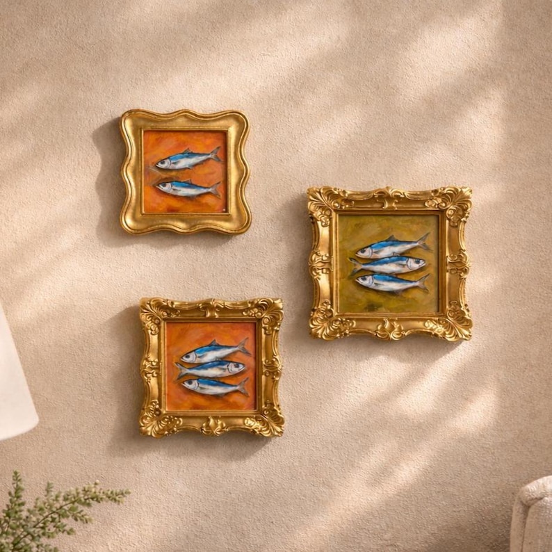 May include: Three framed fish paintings. Each painting features a different arrangement of blue and white fish against a warm orange or green background. The ornate gold frames add a touch of elegance to the artwork.