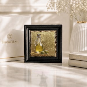 May include: Square framed oil painting of an olive oil bottle with olives. The painting has a gold background and a black frame. The painting is next to a white box with the text "DariaOilArt".