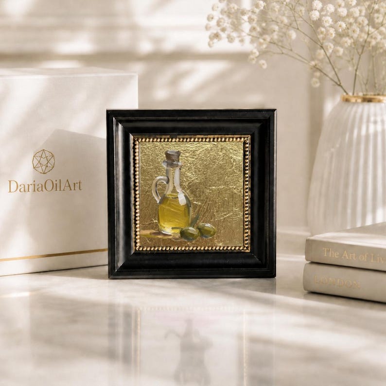 May include: Square framed oil painting of an olive oil bottle with olives. The painting has a gold background and a black frame. The painting is next to a white box with the text "DariaOilArt".